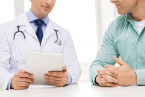 médico usando jaleco sentado em mesa com paciente homem