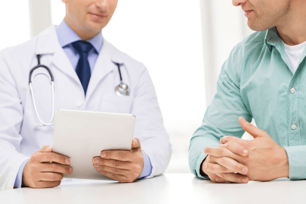 médico usando jaleco sentado em mesa com paciente homem