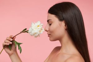 moça em posição perfil nariz bonito cheirando uma flor