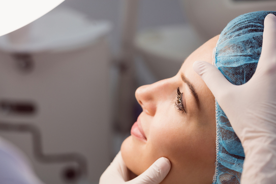 médico examinando rosto da paciente com mãos com luva como escolher o cirurgião plástico para a rinoplastia