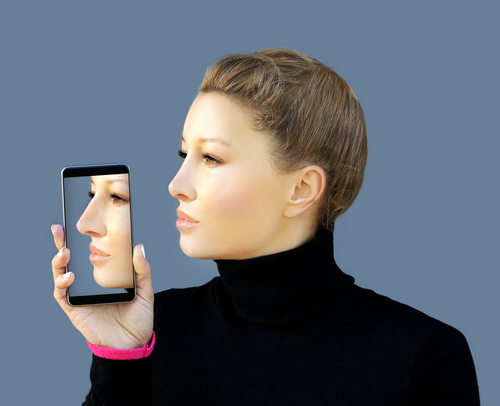 rosto de mulher de perfil com celular na mão mostrando antes e depois da Rinoplastia