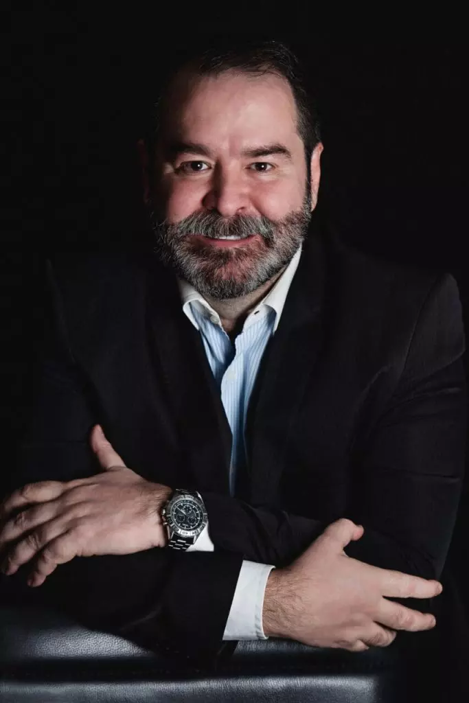 foto Dr. Iran sorrindo fundo preto terno preto camisa azul clara braços cruzados